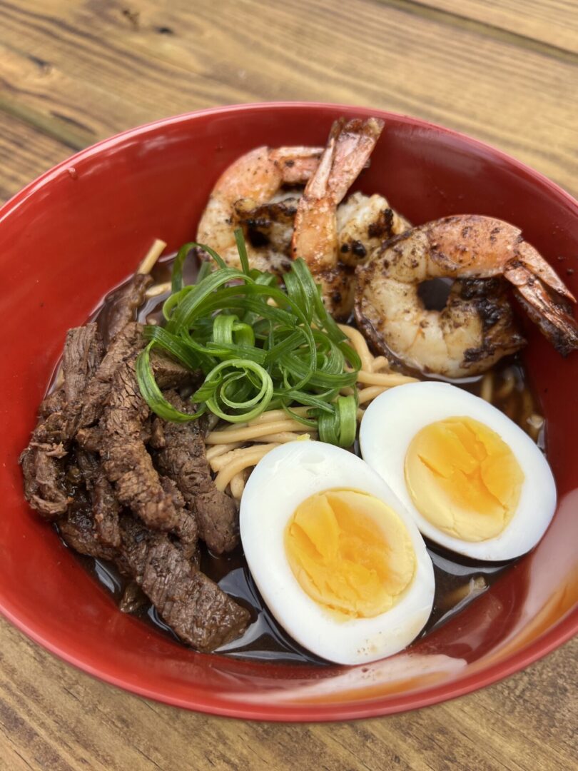 A bowl of food with shrimp, eggs and meat.