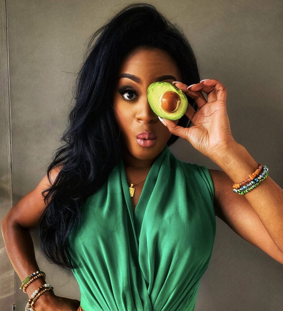 Woman playfully covers eye with avocado.